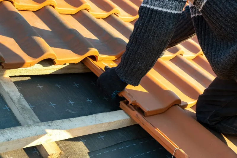 Roofer fitting new clay tiles over battens and membrane